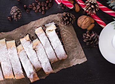 Slice of fresh baked homemade strudel with poppy seeds and  sugar powder,  on a black background  and fir branches. Cocoa with murshmelou. Christmas, winter still life