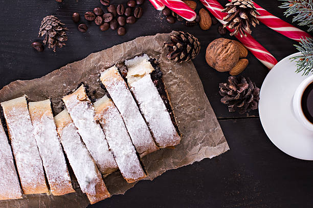 Slice of fresh baked homemade strudel with poppy seeds and  sugar powder,  on a black background  and fir branches. Cocoa with murshmelou. Christmas, winter still life